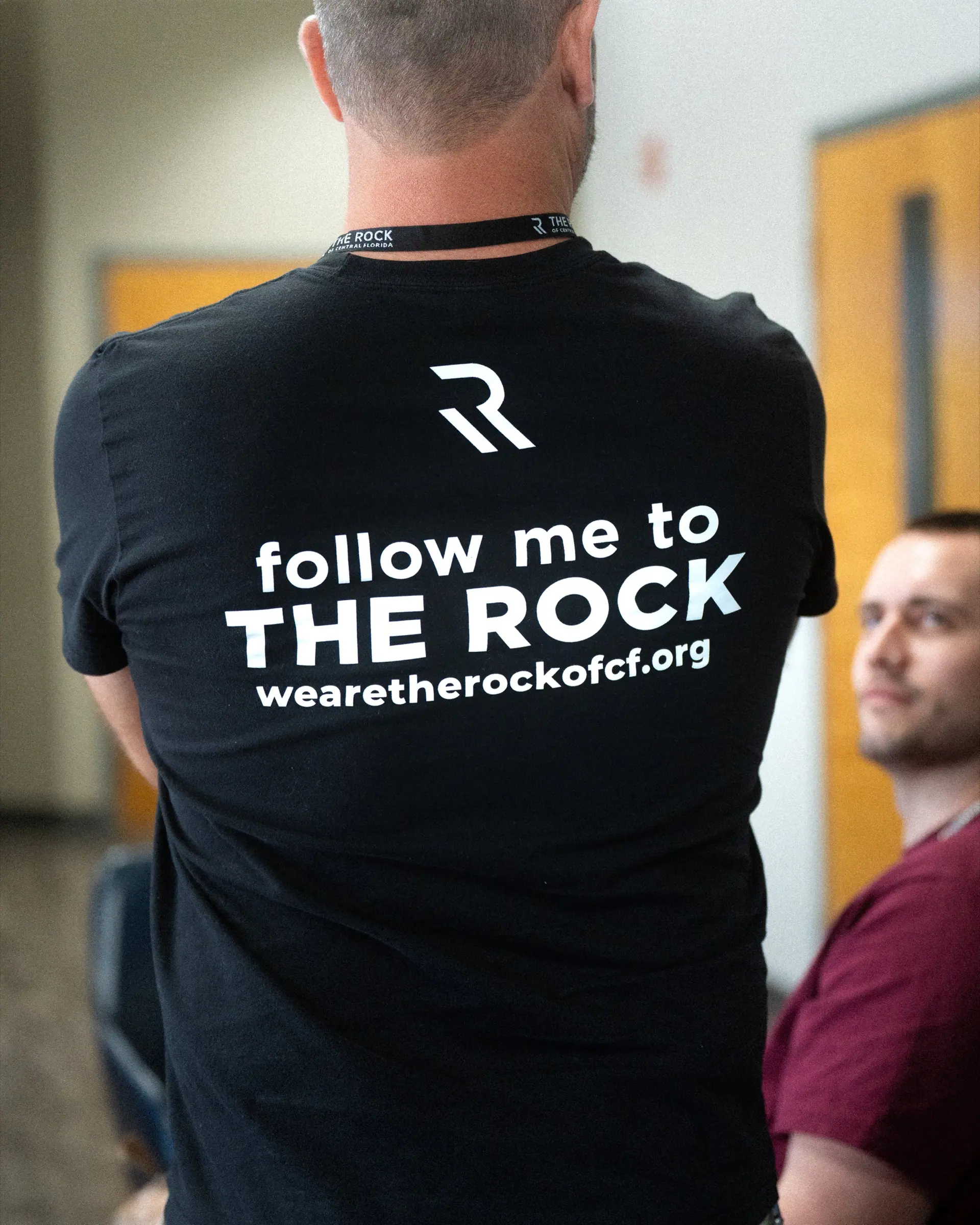 The back of a black tee reading follow me to The Rock