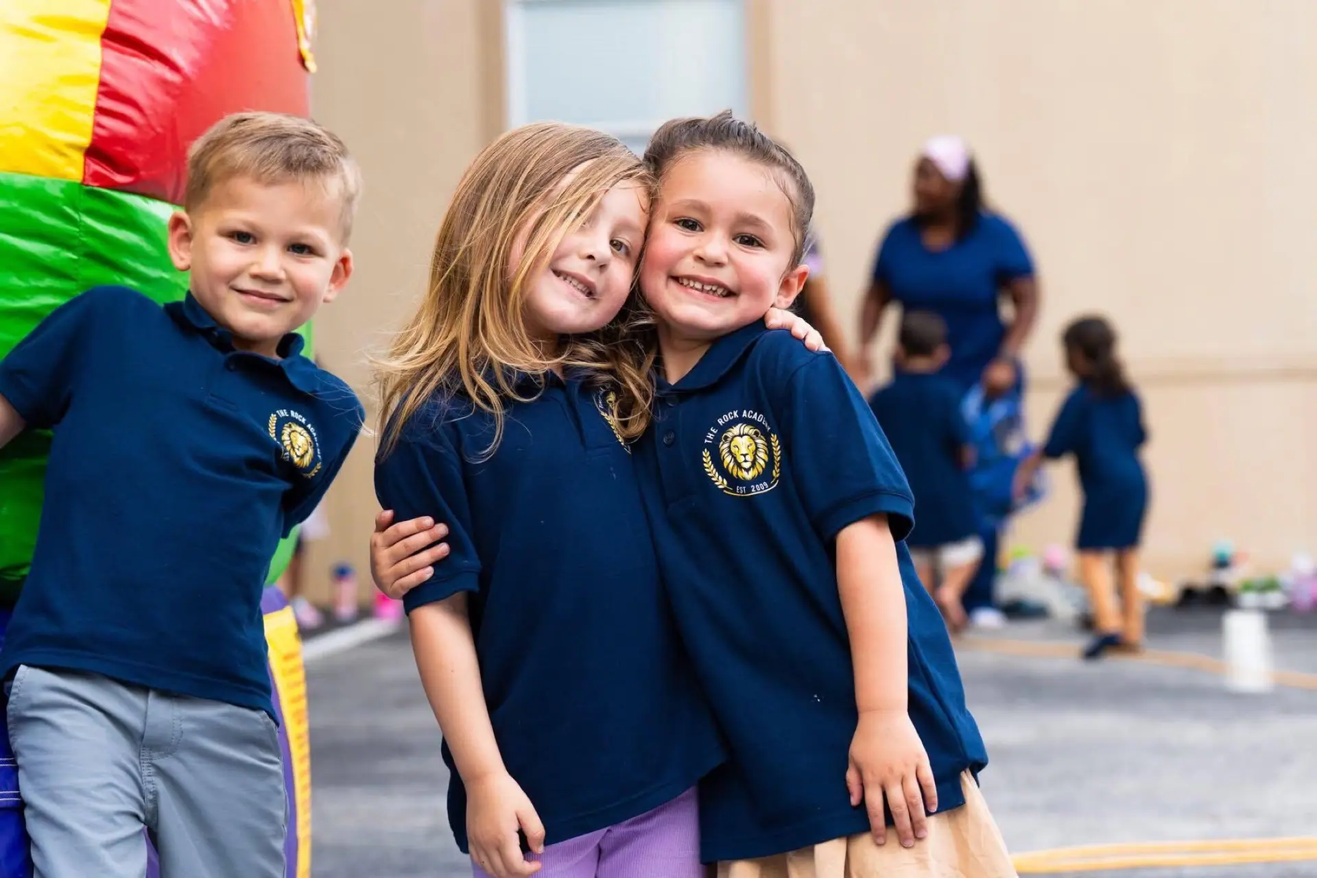 Three young Rock Academy students in navy polos hugging