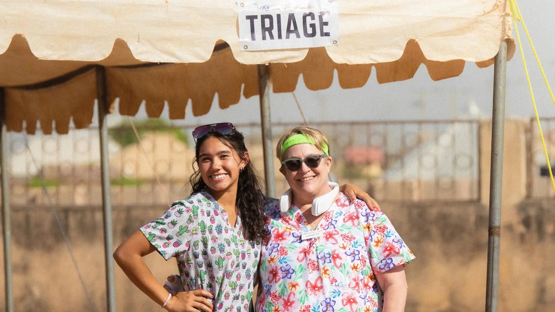 Two volunteers in scrubs at a triage tent